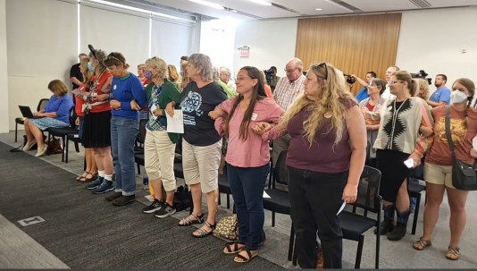photo from July 12 Iowa Utilities Board meeting showing landowners, climate justice fighters and others linking arms in solidarity against the proposed pipelines