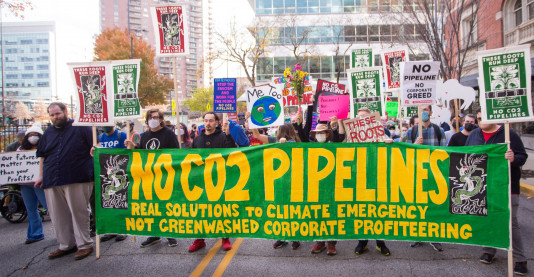 photo from Nov. 9 pipeline protest with people marching and holding large banner reading "no CO2 pipelines. real solutions to climate emergency, not greenwashed corporate profiteering"