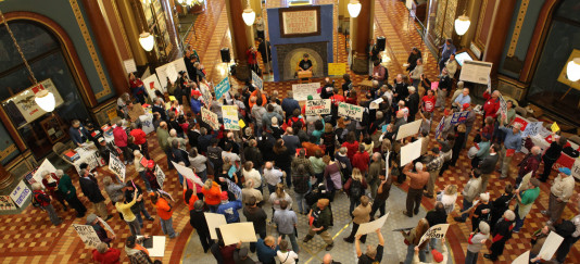 photo from a rally at the statehouse showing hundreds of people holding signs on the first floor rotunda